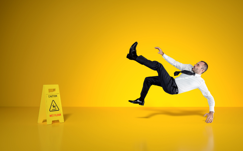 A man is slipping and falling near a 'caution: wet floor' sign
